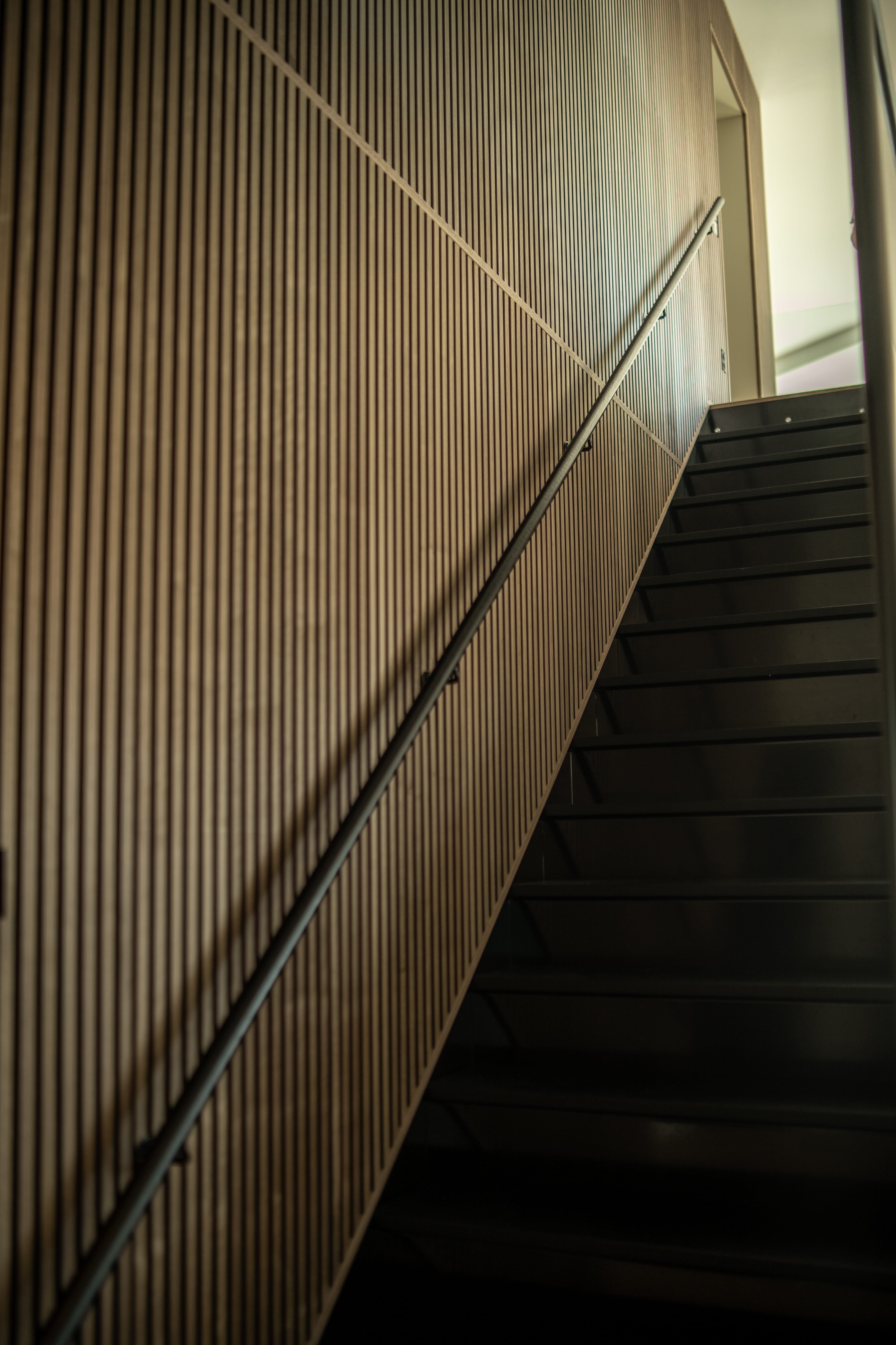 A modern staircase with black steps is complemented by a vertical acoustic slatwall panel, viewed from below at an angle for a minimalist Nordic appearance.
